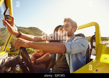 Woman kissing man et en tenant son téléphone mobile selfies. Couple on road trip, homme conduisant une voiture buggy sur une journée d'été. Banque D'Images