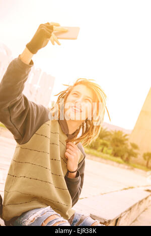 Portrait de jeune homme à l'extérieur des cheveux rasta smiling with smart phone dans un concept de vie avec un filtre appliqué à chaud Banque D'Images