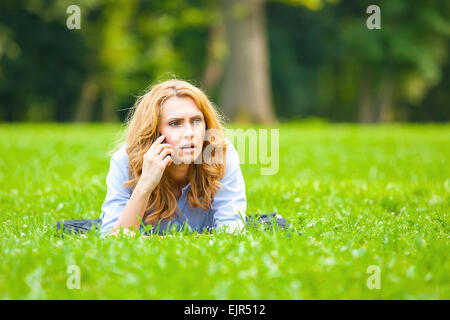 Belle jeune femme allongée dans l'herbe verte et parlant au téléphone cellulaire Banque D'Images