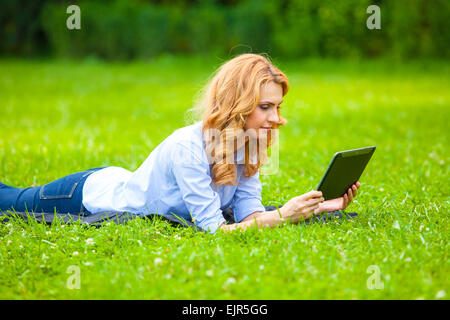 Belle blonde woman lying in grass et à l'aide d'une tablette Banque D'Images