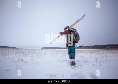 Mixed Race man carrying skis in snowy field Banque D'Images