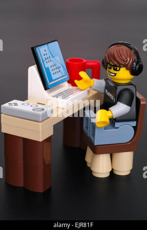 Guy Jeu Vidéo Lego playmobil - 5116 - moto (joueur 1) à sa table avec ordinateur, manette et tasse sur fond noir. Banque D'Images