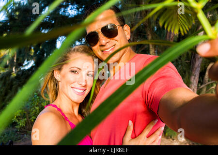 Smiling couple hugging derrière les feuilles de palmier Banque D'Images