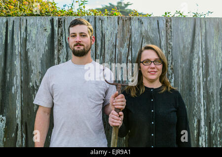 Caucasian couple holding pitchfork près de clôture Banque D'Images