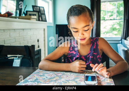 Mixed Race girl using cell phone at table de cuisine Banque D'Images