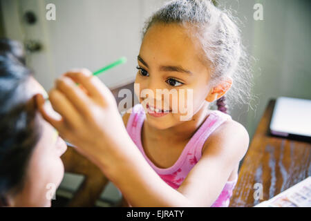 Girl painting visage de la mère à la table de cuisine Banque D'Images