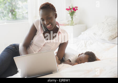Ordinateur portable à l'aide de mère noire près de sleeping baby boy