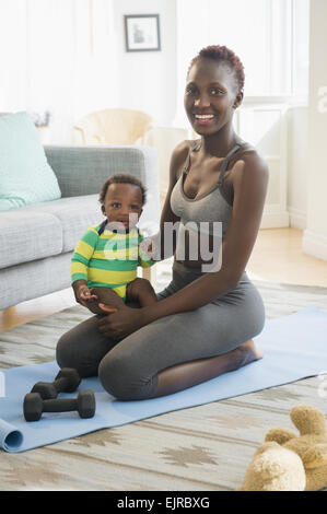 Black Mother holding baby boy sur tapis d'exercice dans la salle de séjour Banque D'Images