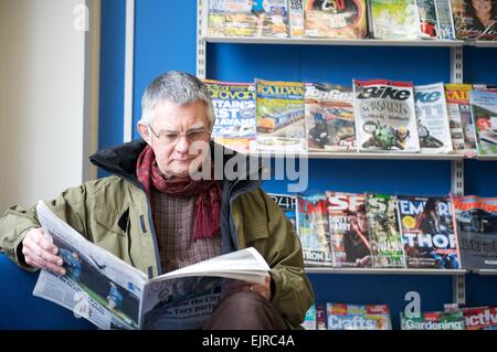 Senior man reading a newspaper dans une bibliothèque publique Banque D'Images