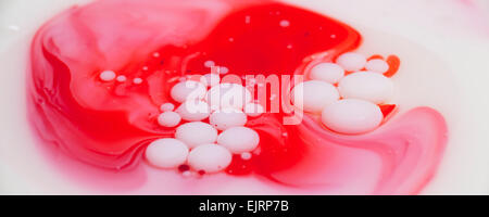 Une couche d'huile minérale sur le dessus de lait avec du lait bulles flottant au-dessus de l'huile ; ajouter du colorant alimentaire Banque D'Images