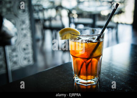 La lumière brille à travers l'arrière d'un grand verre de thé glacé glacée avec une paille noire. Une cale de citron se repose sur le bord de la Banque D'Images