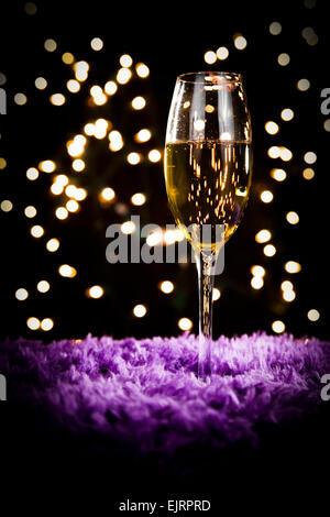 Un verre de champagne se trouve au-dessus d'une surface de la fourrure mauve ; white bokeh en arrière-plan ; parfait pour Noël et Nouvel An ; le rouge à lèvres rouge m Banque D'Images