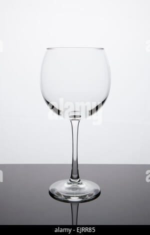 Un verre à vin vide siège sur une surface réfléchissante avec un fond blanc lumineux Banque D'Images