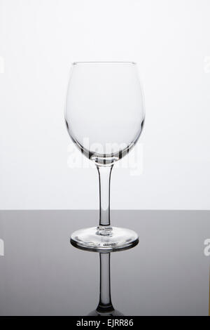 Un verre de vin blanc vide siège sur une surface réfléchissante avec un fond blanc lumineux Banque D'Images