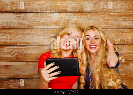 Les jeunes sœurs avec de longs cheveux blonds, faire du PC tablette selfies. Girl smiling et montrant des émotions positives. Banque D'Images