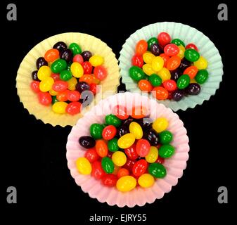 Fruit jelly beans dans beaucoup de couleurs dans les tasses de papier sur un fond noir. Banque D'Images