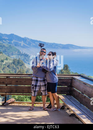 Un jeune couple en vacances prendre un autoportrait à l'aide d'un bâton selfies avec leur smartphone à Big Sur, en Californie. Banque D'Images