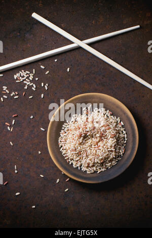 Riz brun non cuit sur une plaque en céramique avec baguettes en bois brun sur surface métallique. Vue d'en haut. Banque D'Images