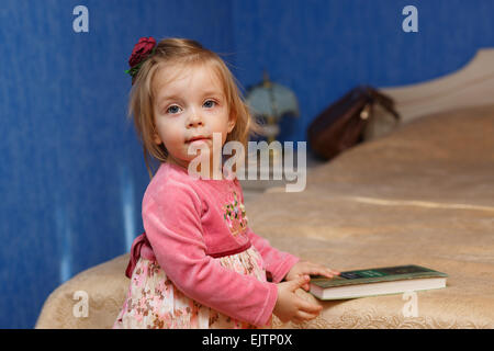 Petite fille mignonne va lire un livre dans la chambre. Le concept de l'éducation dans les années préscolaires. Banque D'Images