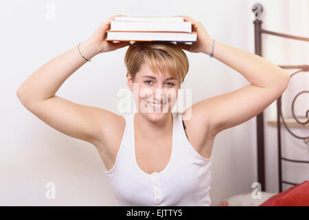 Jolie jeune femme heureuse de prendre une pause dans le cadre de ses études collégiales balancing books sur sa tête quand elle regarde la caméra avec un w Banque D'Images