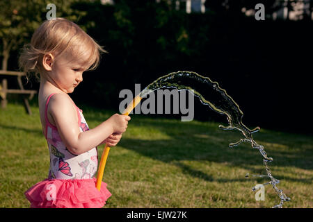 Jeune fille de pulvériser de l'eau d'un tuyau dans le jardin en été. Banque D'Images