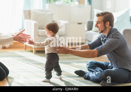 Heureux parents aidant les petits fils (2-3 ans) Balade dans la salle de séjour Banque D'Images