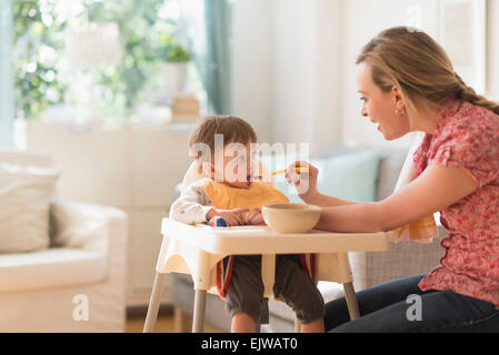 L'alimentation de la mère petit garçon (2-3 ans) dans une chaise haute Banque D'Images