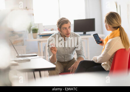 Jeune homme et femme discuter at desk in office Banque D'Images