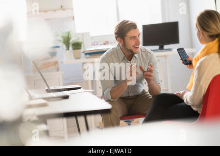 Jeune homme et femme discuter at desk in office Banque D'Images