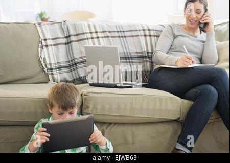 Mère et fils (6-7) assis dans la salle de séjour avec ordinateur portable et tablette Banque D'Images