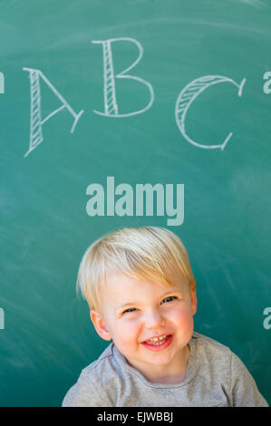 Boy (2-3) smiling in front of blackboard avec lettres ABC écrit dessus Banque D'Images