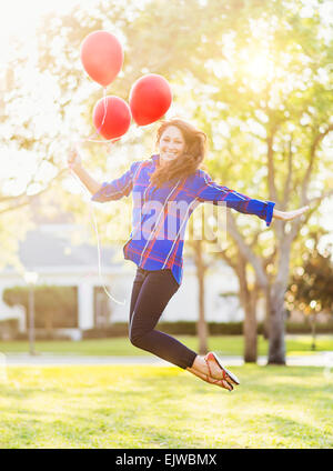 USA, Floride, Jupiter, Woman holding balloons jumping Banque D'Images