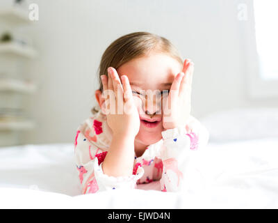 Girl (2-3) lying on bed pulling funny face Banque D'Images