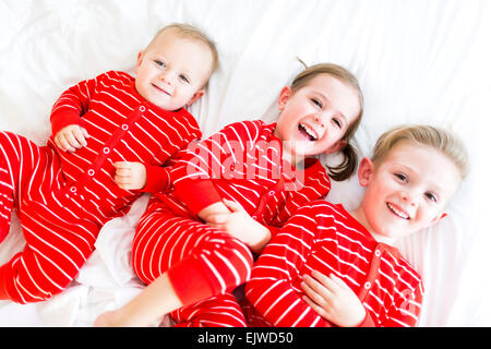Girl (4-5) et deux frères (6-7) lying on bed en pyjama rayé Banque D'Images