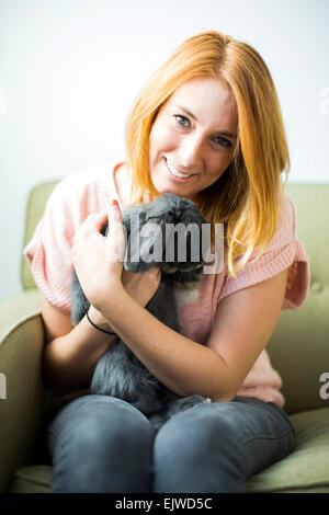 Femme assise sur un canapé embrassant lapin Banque D'Images