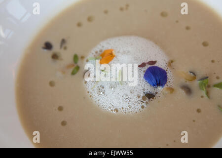 Soupe de chou-fleur caramélisé, avec mousse de raifort et garnir de fleurs sauvages, servi dans un bol blanc. Banque D'Images