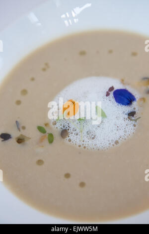 Soupe de chou-fleur caramélisé, avec mousse de raifort et garnir de fleurs sauvages, servi dans un bol blanc. Banque D'Images