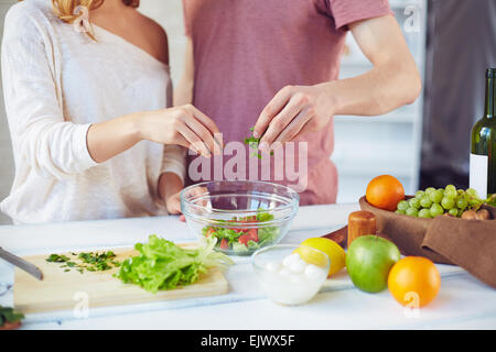 Mains de jeune couple l'ajout de persil dans le bol à salade végétarienne fraîche Banque D'Images