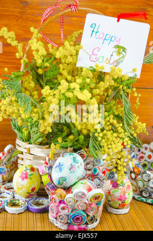 Papier fait main colorés avec des paniers remplis d'oeufs de Pâques et decoupage mimosa sur une table en bois Banque D'Images