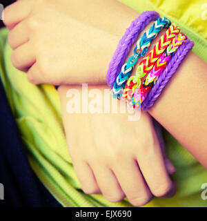 Les mains de l'enfant aux couleurs arc-en-ciel en caoutchouc loom band bracelets tendance, accessoires de mode. Vintage Retro filtre photo tonale Banque D'Images