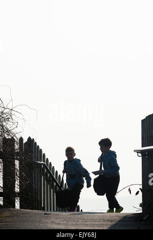 Deux jeunes enfants d'âge primaire des enfants (garçons) en silhouette à l'école à pied sur un froid matin d'hiver, le Pays de Galles UK Banque D'Images