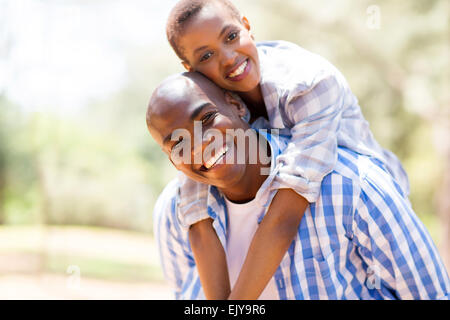 Pretty African woman piggyback ride on petit ami à l'extérieur Banque D'Images