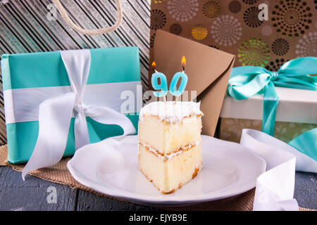 Tranche de gâteau d'anniversaire avec '90' bougie pour quatre-vingt-dixième anniversaire placé avec des cadeaux et cartes. Banque D'Images