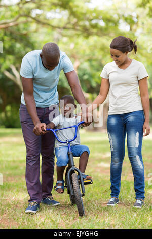 Les jeunes parents à enseigner à leurs fils à faire du vélo au parc Banque D'Images