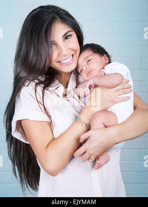 Portrait de belle mère joyeuse avec mignon bébé sur les mains sur fond de mur bleu, profitant de la parentalité Banque D'Images