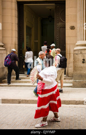 Scène de rue dans la Vieille Havane, Cuba. Femme avec ventilateur chanter comme elle vend des arachides dans la rue devant une banque. Banque D'Images