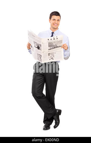 Portrait d'un bel homme tenant un journal et appuyé contre un mur isolé sur fond blanc Banque D'Images