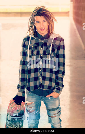 Portrait de jeune homme avec des cheveux rasta et skateboard dans un concept de vie filtre appliqué à chaud Banque D'Images