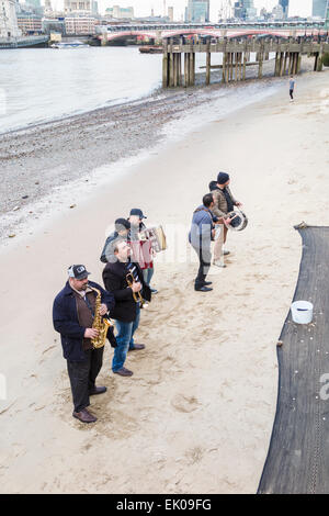 Une bande d'amuseurs de l'exécution musicale pour des conseils sur une plage de sable à marée basse sur la rive sud de la rivière Thames Embankment, London Borough of Southwark, SE1 Banque D'Images