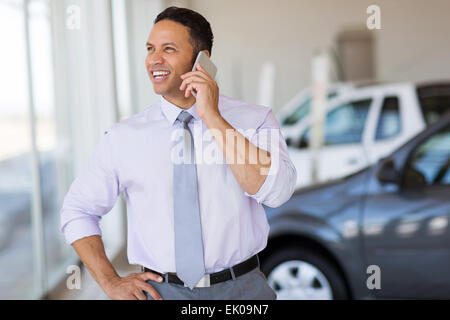 Beau car salesman talking on cell phone in showroom Banque D'Images